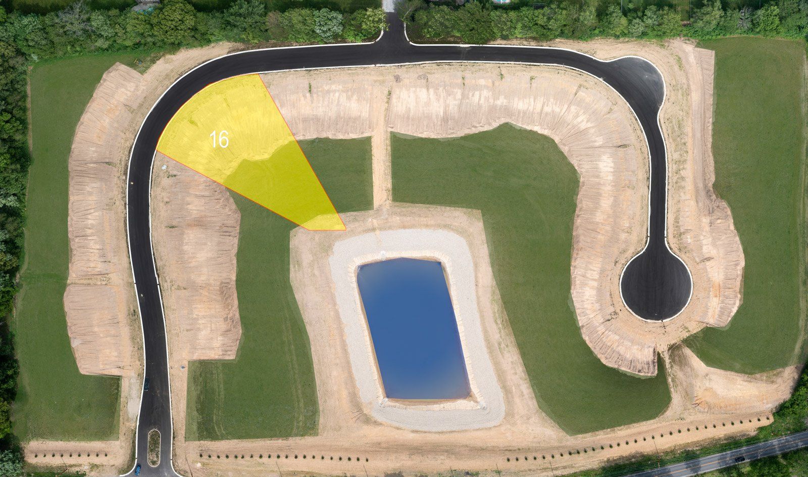 Aerial view of a construction site with roads and a water retention pond, yellow highlight indicates an area of interest.