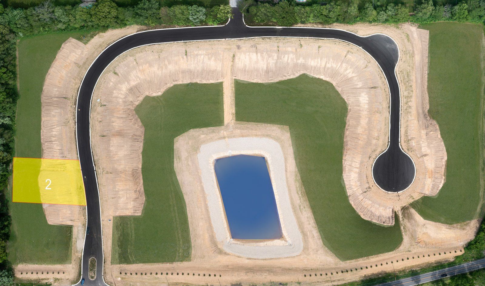 Aerial view of a planned residential development with roads, a retention pond, and undeveloped lots; one highlighted in yellow.