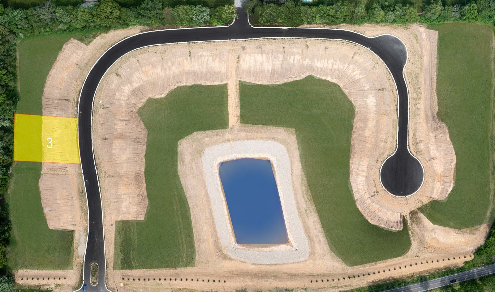 Aerial view of a construction site with roads, a pond, and graded land, marked with a yellow rectangle.