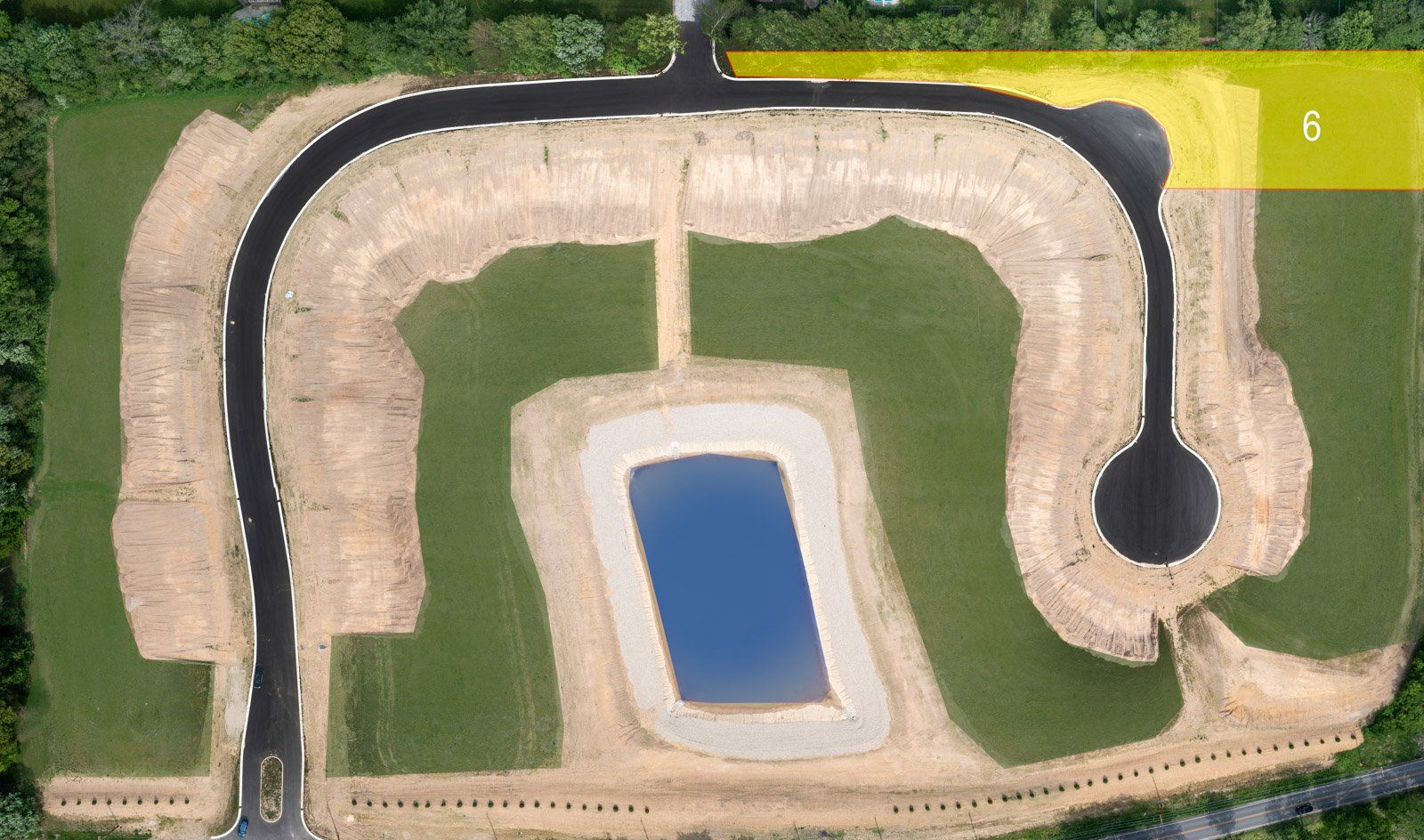 Aerial view of a new housing development with roads, a pond, and cleared land.