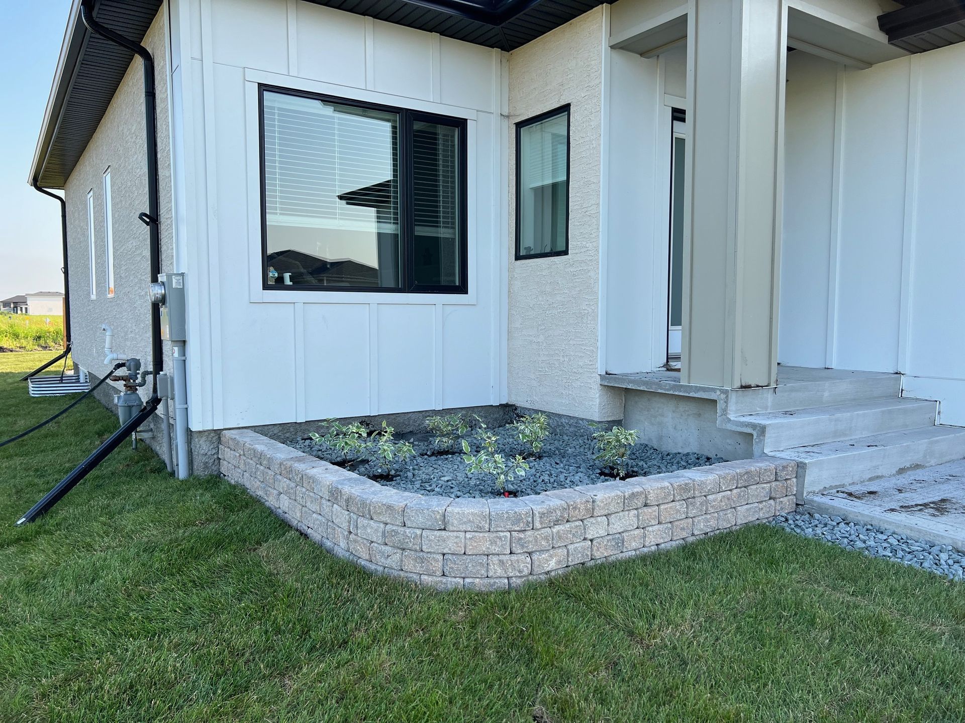 A low, curved stone wall borders a green grass lawn, with colorful garden plants growing along the top.