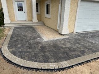 A curved paver walkway with a light-colored gravel border leading to the front door and garage of a suburban home.