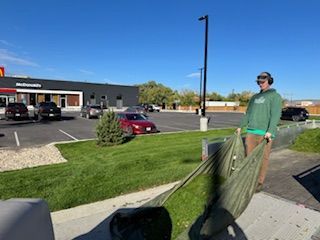 A person in a green hoodie drags a large, full leaf tarp across a grass lawn in front of a McDonald’s parking lot.