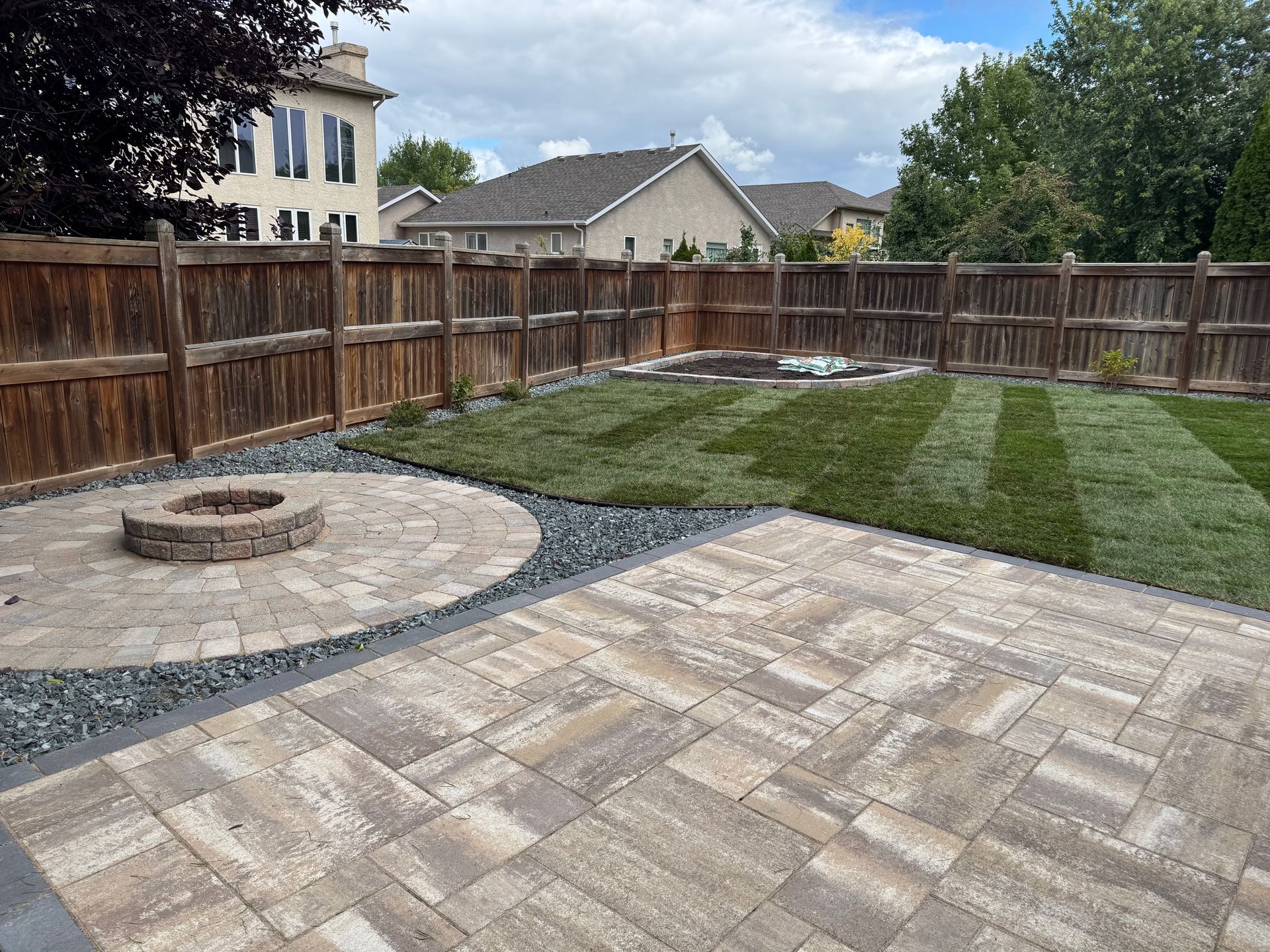 A gravel path leads through a lush green park toward flowerbeds and a distant structure under a cloudy sky.