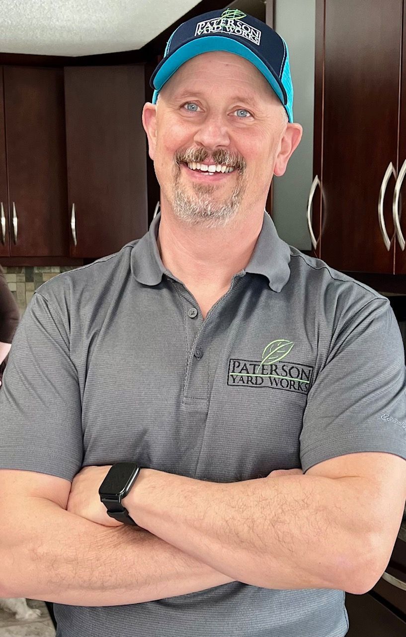A modern two-story home with a paved patio and steps in the foreground, framed by two outdoor post lamps under a blue sky.