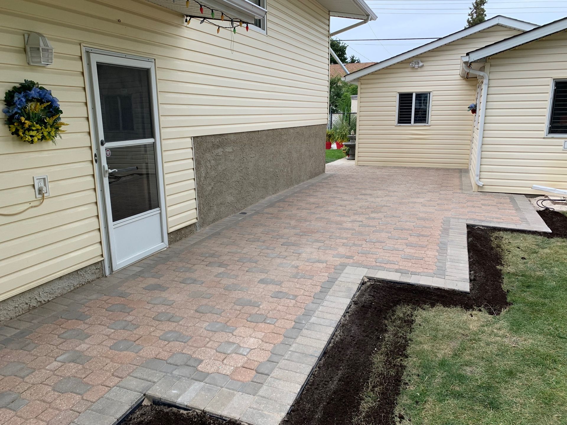 A newly installed paver patio with a zig-zag border edge adjacent to a house with cream siding and a white screen door.