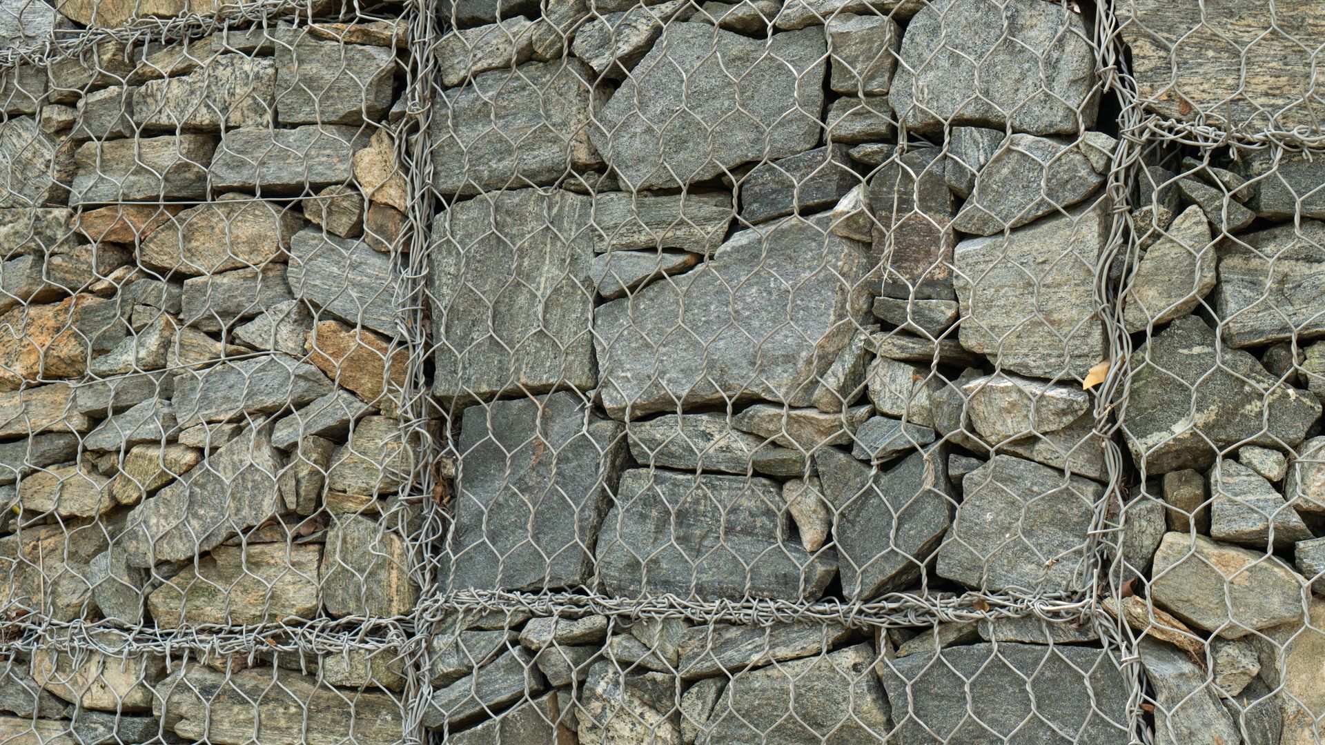 A gabion wall constructed from stacked gray rocks secured inside a metal wire mesh grid.