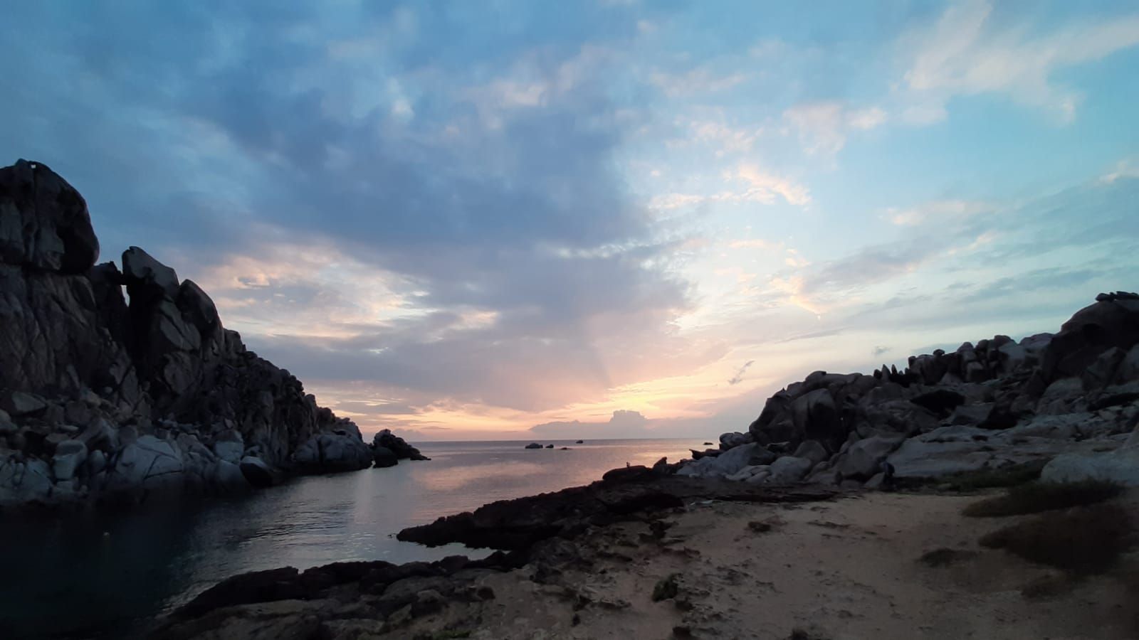 Costa rocciosa al tramonto, cielo dai colori tenui.