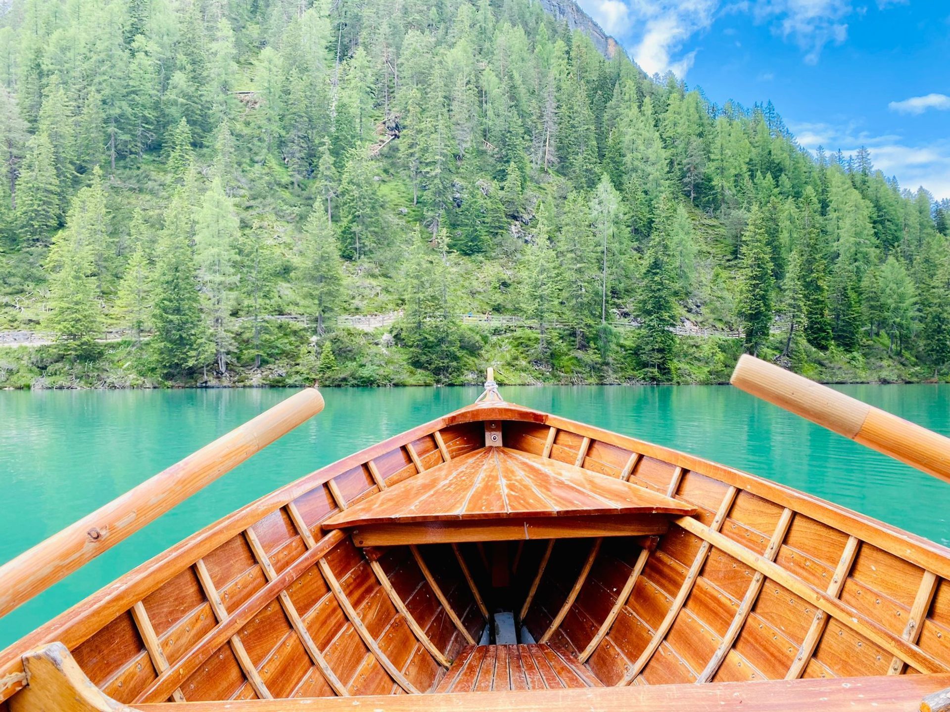Barca a remi in legno su un lago turchese con montagne e alberi sullo sfondo.