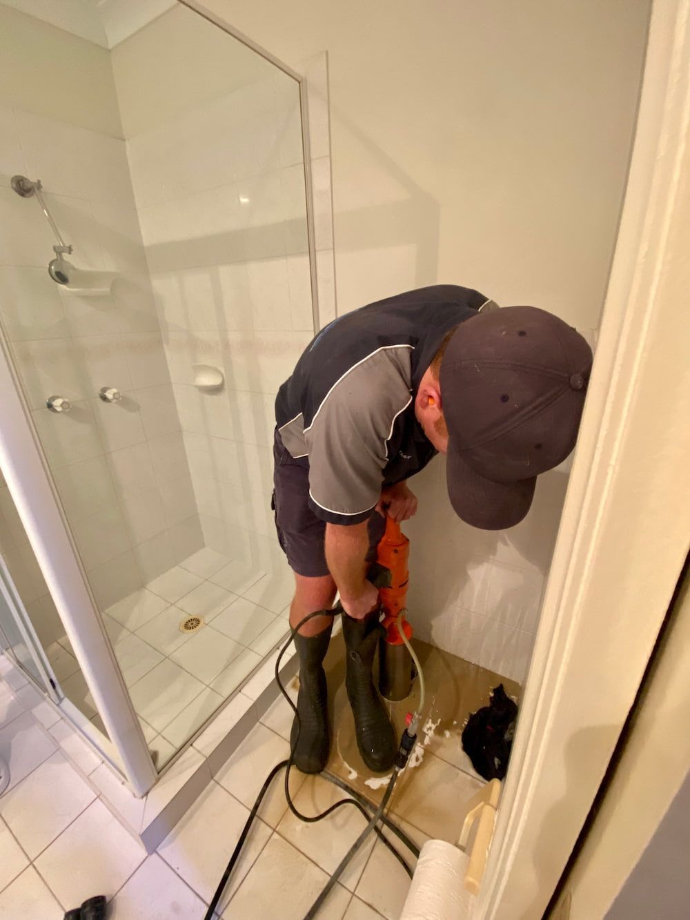 A Man Is Working In A Bathroom With A Drill — Plumbmasters In Burleigh Heads, QLD