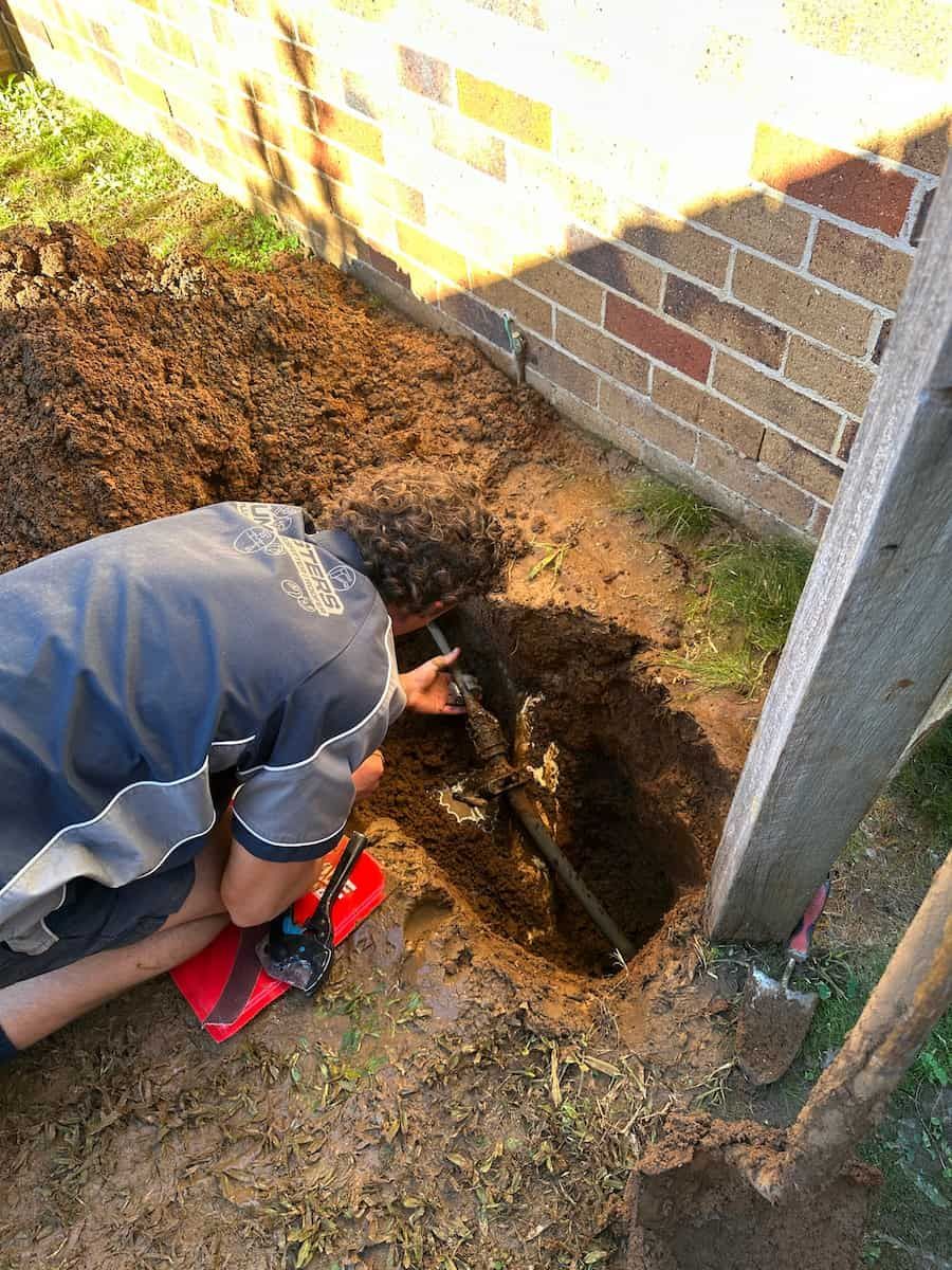 A Man Is Digging A Hole In The Ground Next To A Brick Wall — Plumbmasters In Burleigh Heads, QLD
