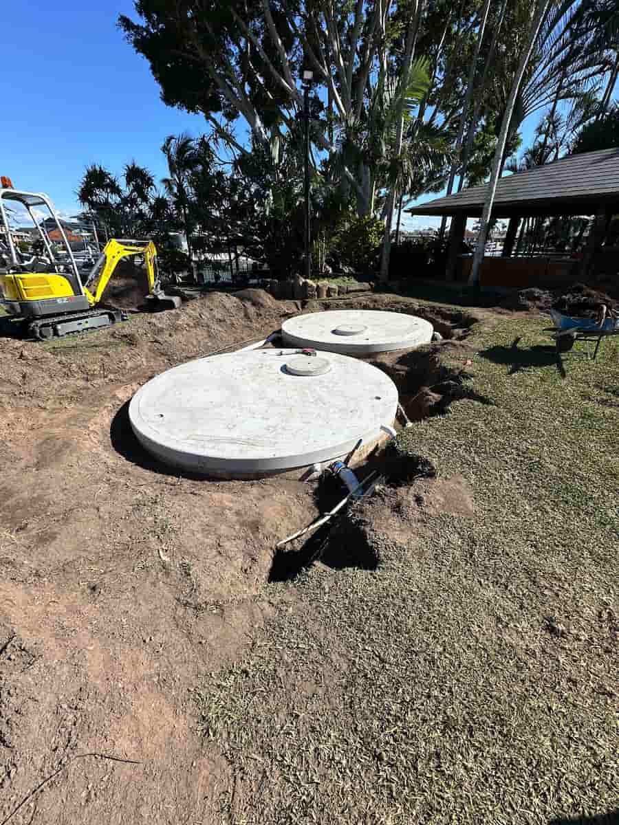 A Yellow Excavator Is Digging A Hole In The Ground To Install A Septic Tank — Plumbmasters In Mermaid Waters, QLD