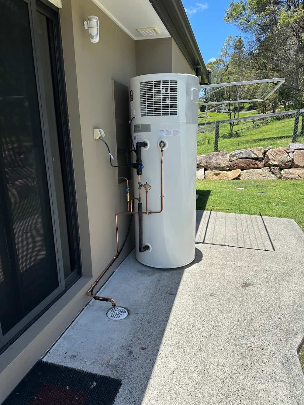 A White Water Heater Is Sitting On The Side Of A House — Plumbmasters In Robina, QLD