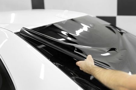 A person is wrapping a car window with a black film.