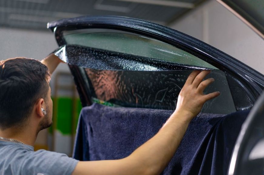 A man is applying tinted window film to a car window.