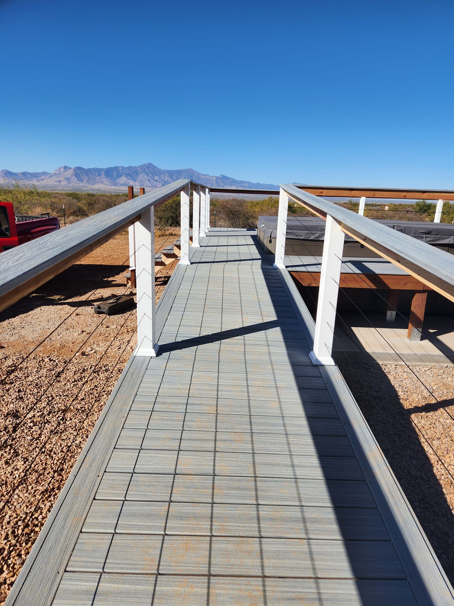 Wooden ramp with handrails extends from foreground toward a mountainous landscape under a blue sky.