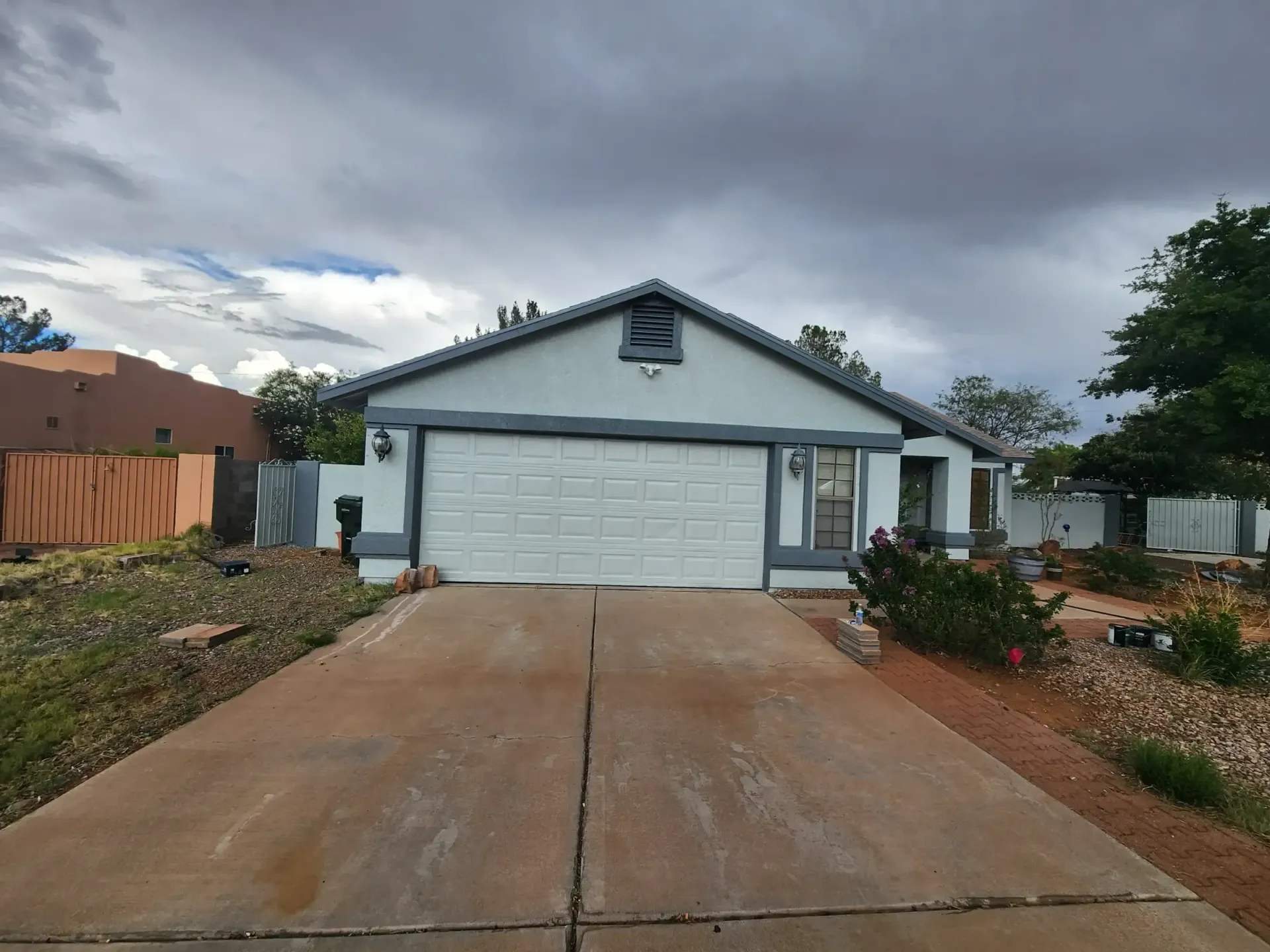 A white house with a gray garage door under a cloudy sky. The driveway is cracked.