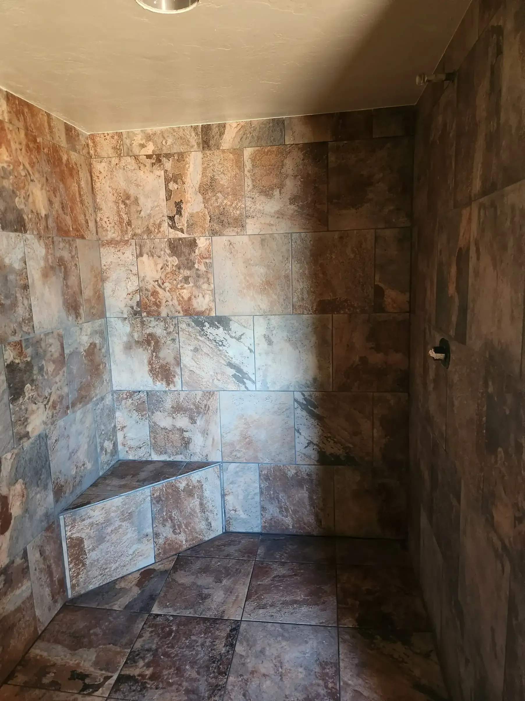 Shower stall with stone-like tile walls and a built-in corner seat; unfinished.
