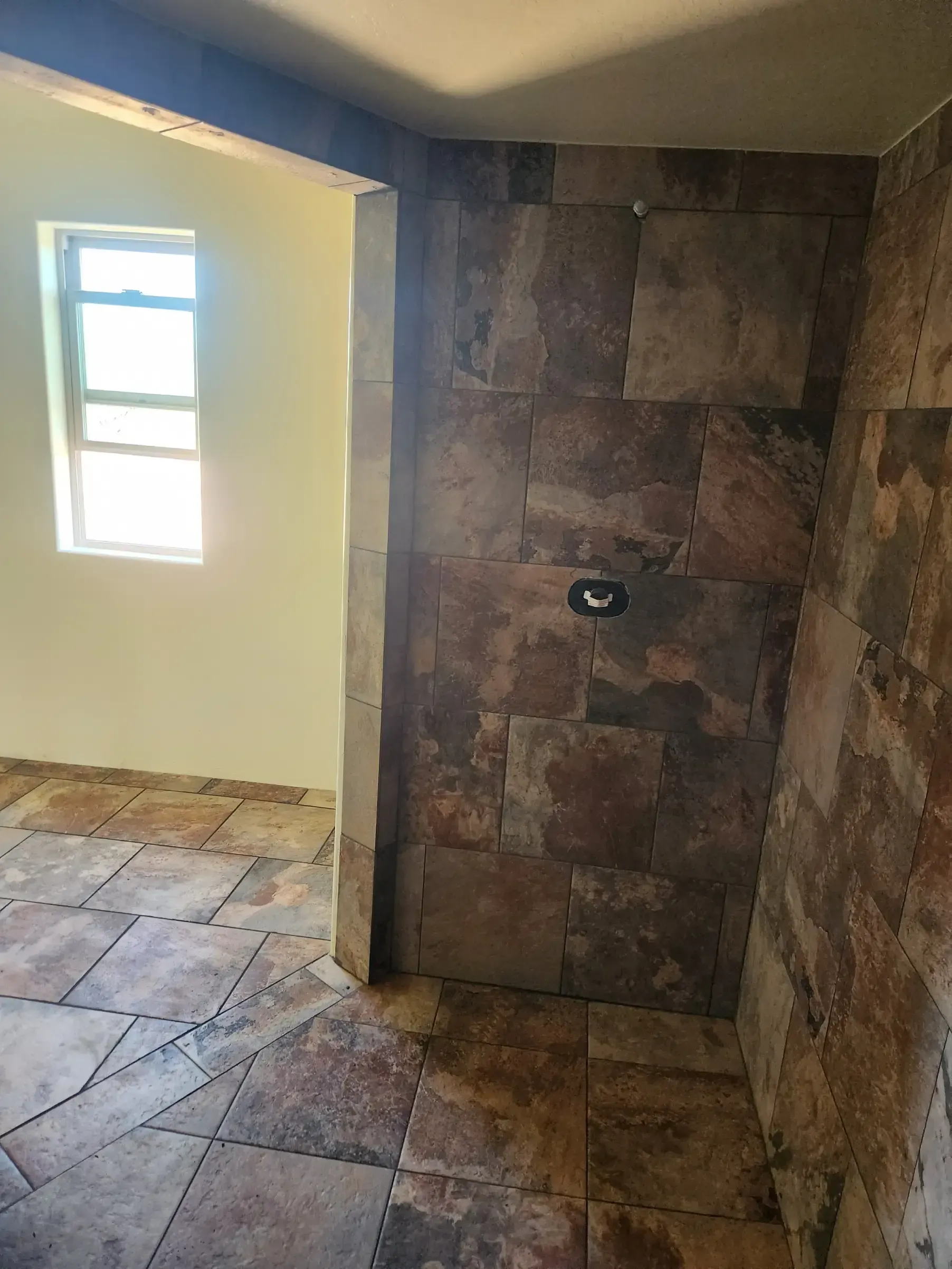 Stone tile doorway leads to a room with a window, tile floor and off-white walls.