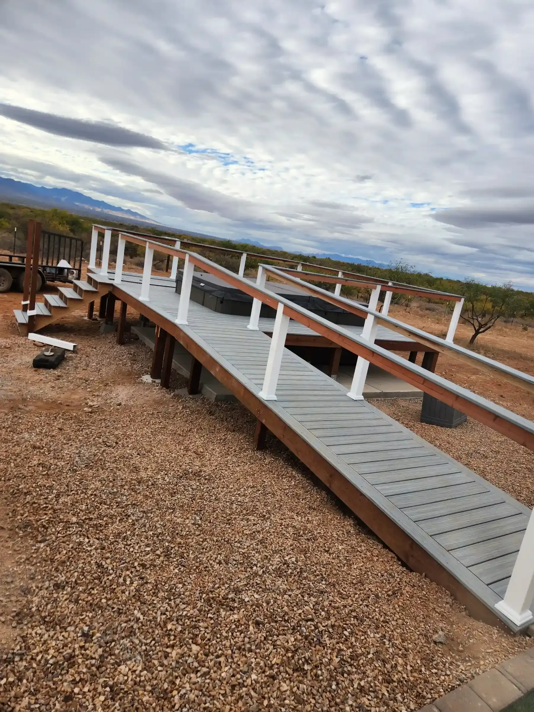 A wooden ramp with railings extends into a yard with gravel and cloudy sky.