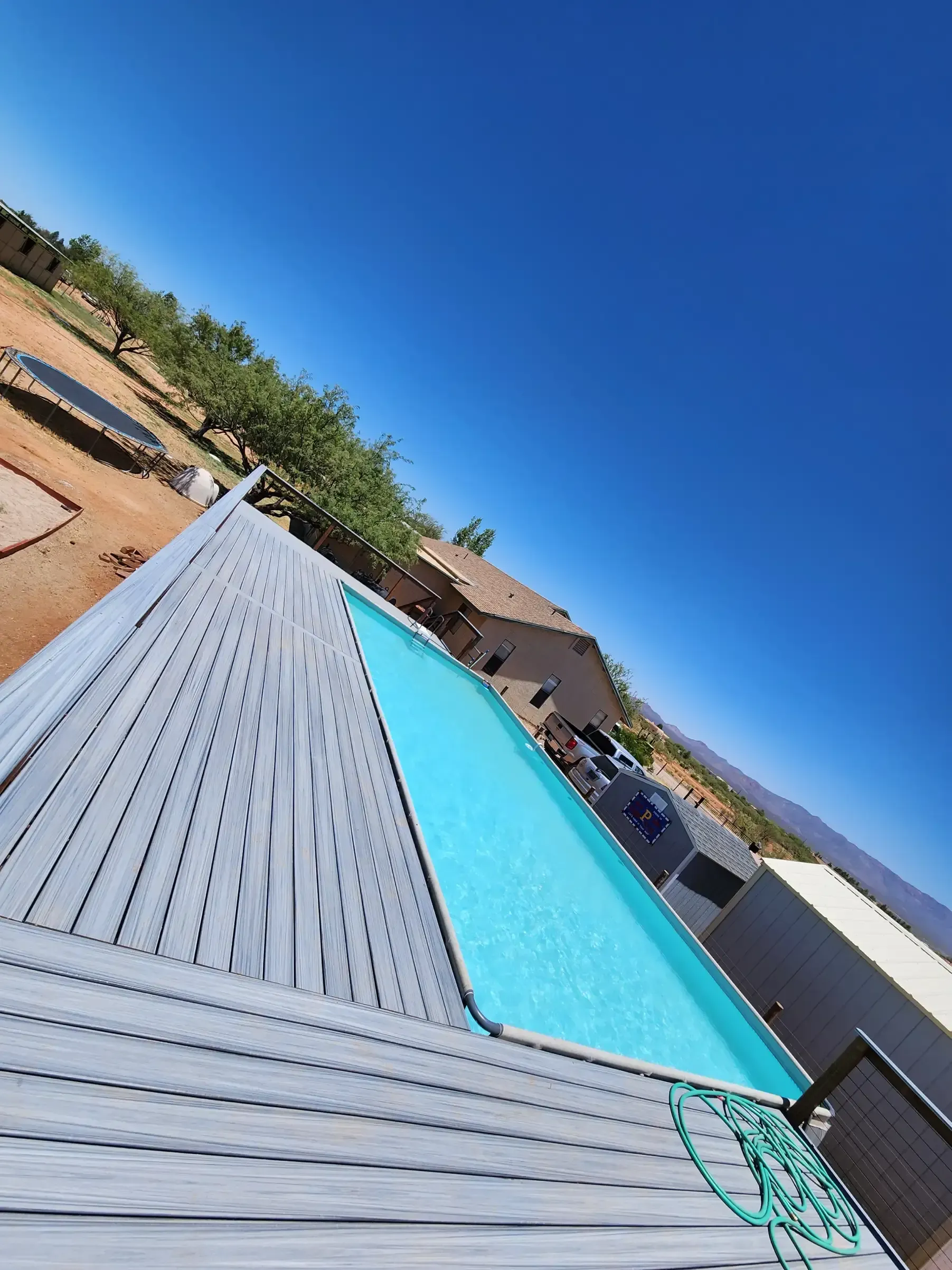 Pool with wooden deck under a bright blue sky.
