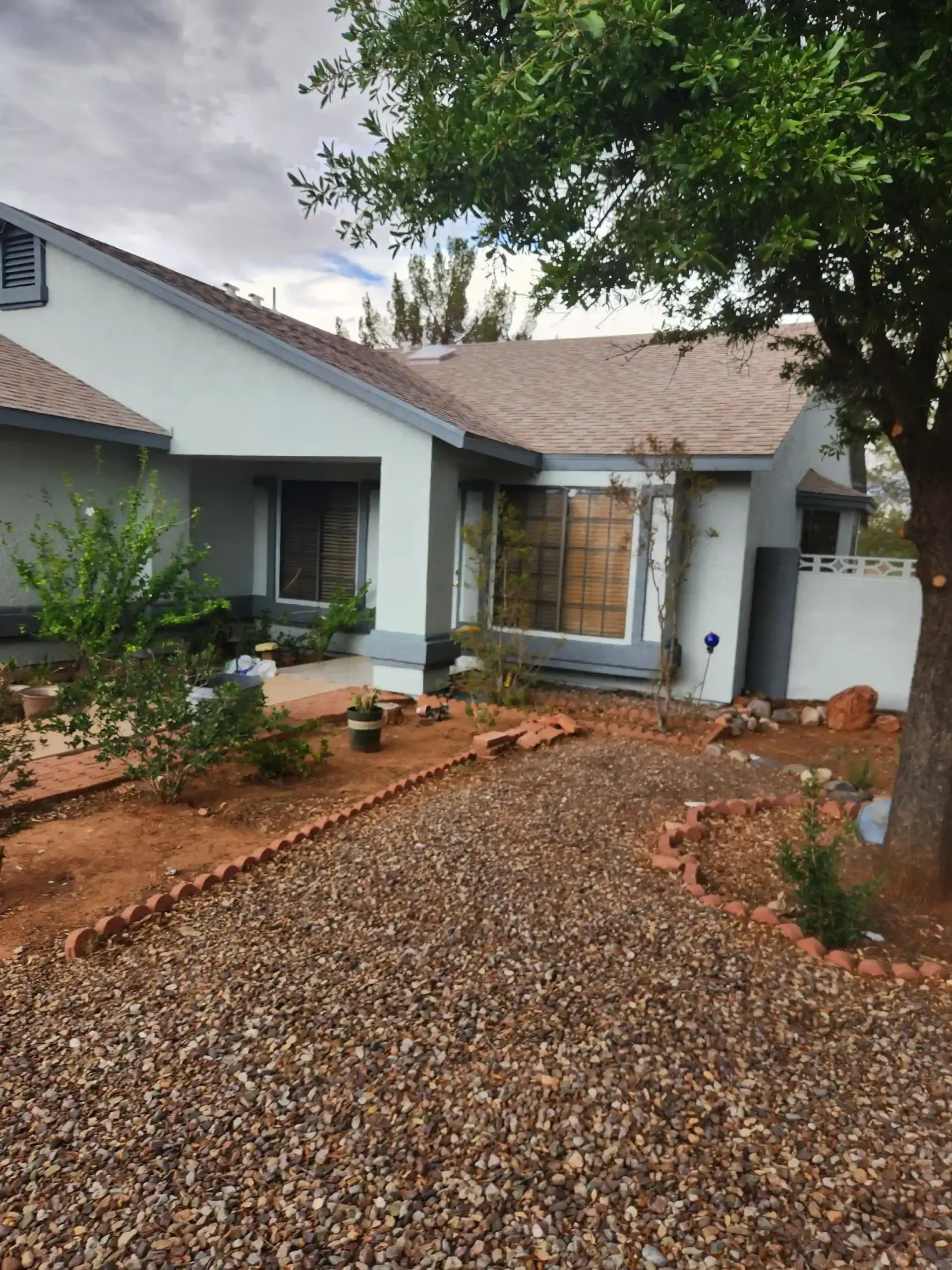 House exterior with gravel path, red rock landscaping, and a tree.
