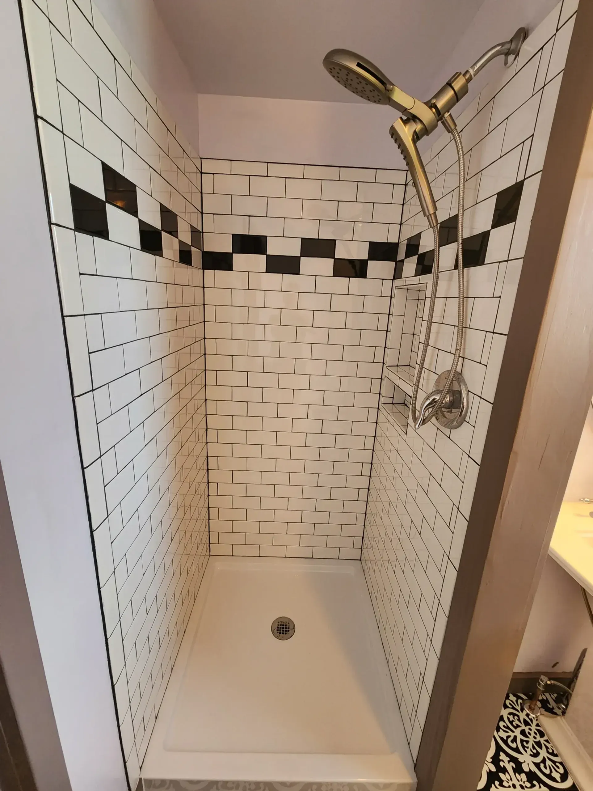 Shower with white and black tile design, silver showerhead, and white base.