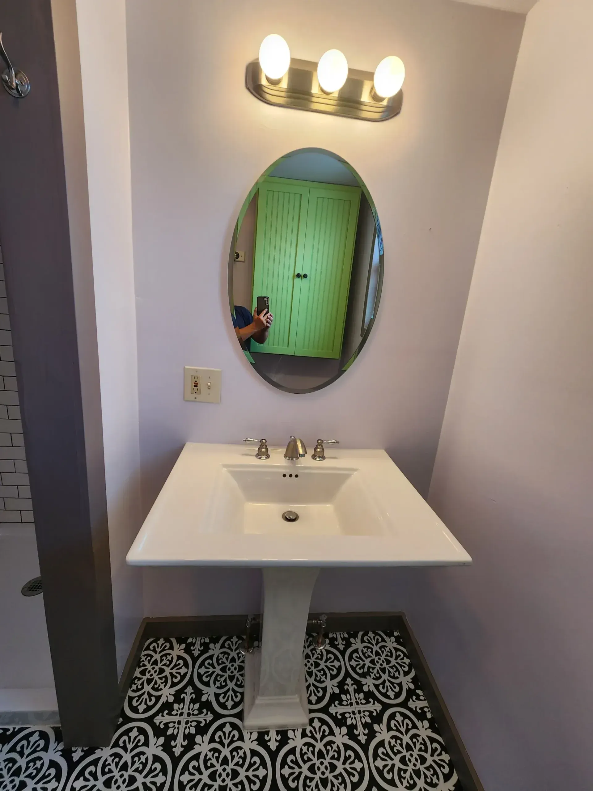 Bathroom with white pedestal sink, oval mirror, and patterned floor.