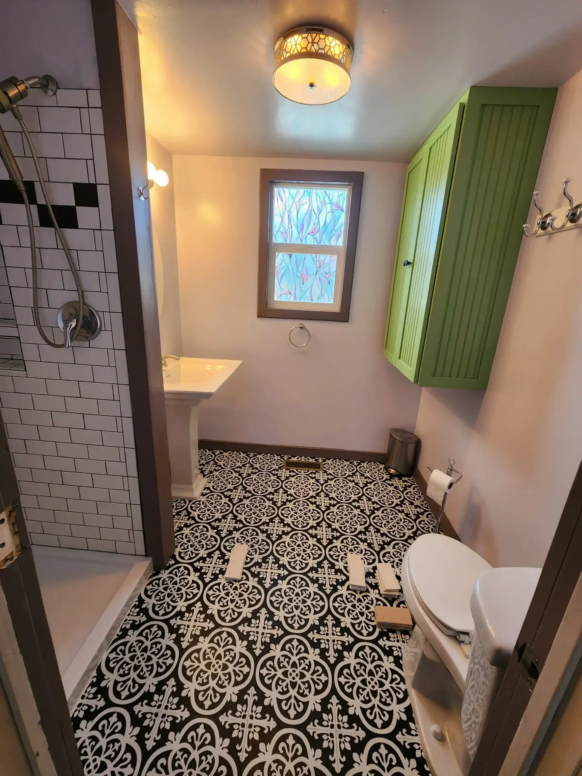 Bathroom with black and white patterned floor tiles, green cabinet, and shower.