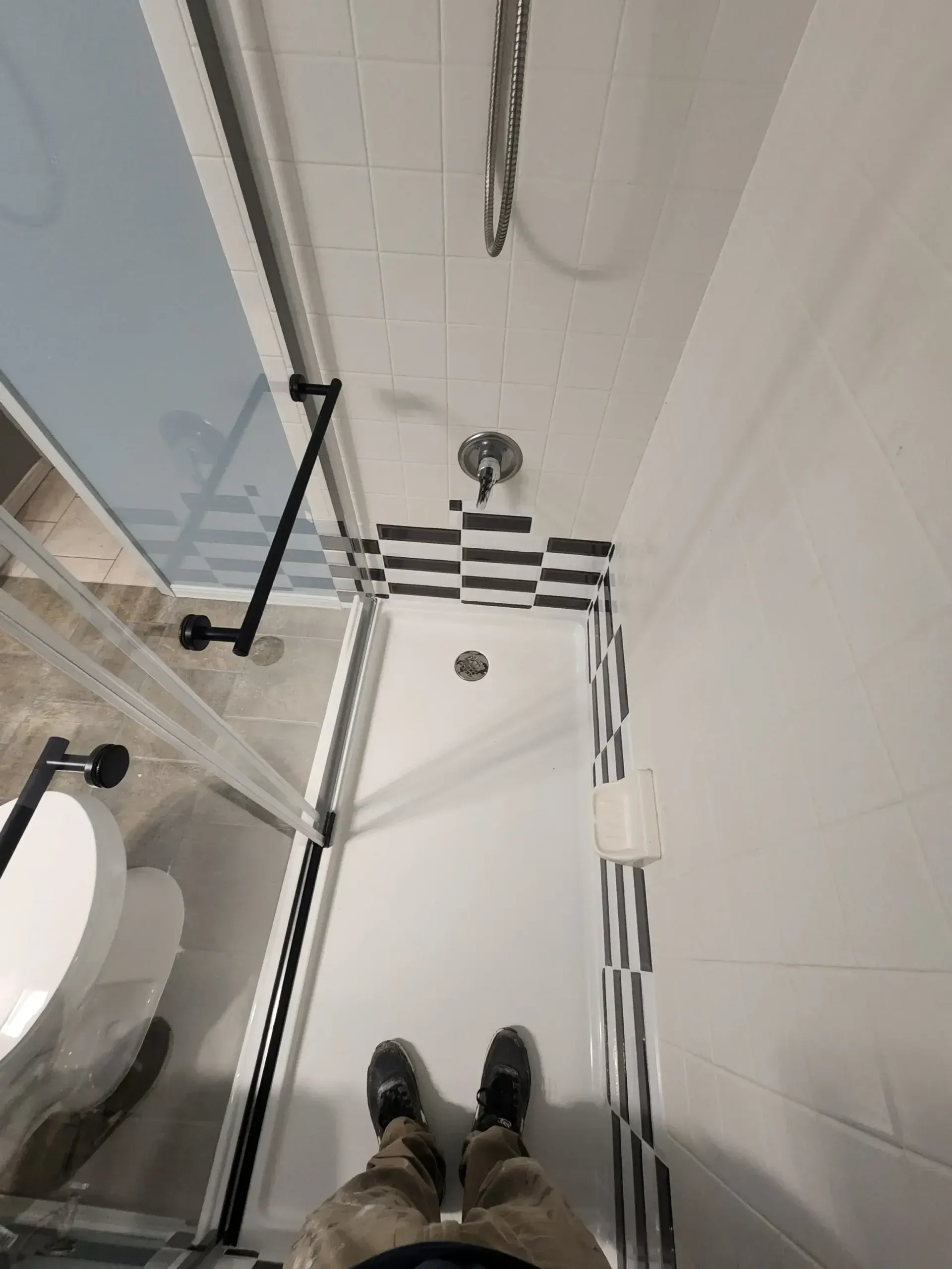 Shower stall with glass door, black and white tiled accents, and a person's feet.