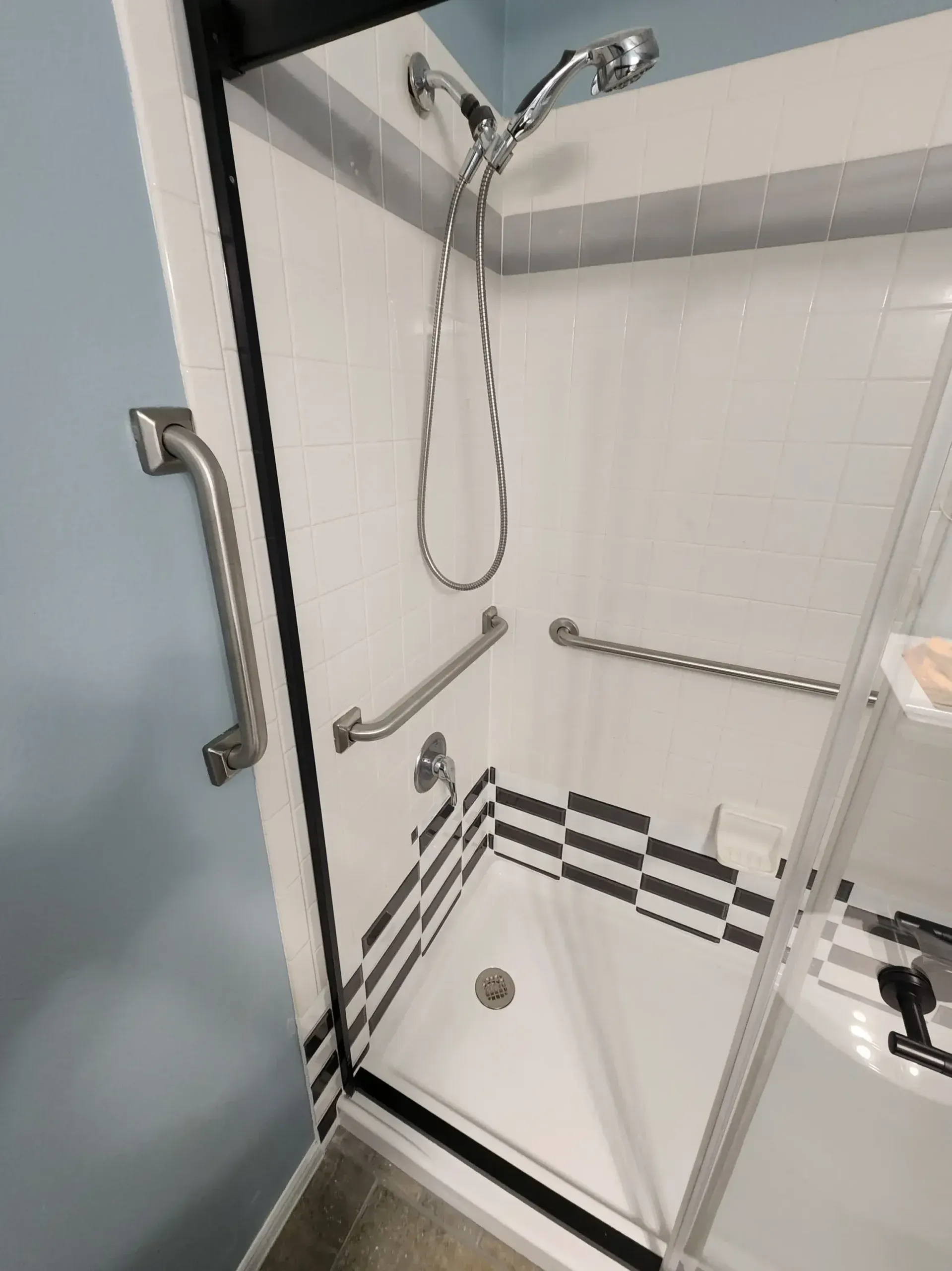 Accessible shower with grab bars and black/white tile accent.