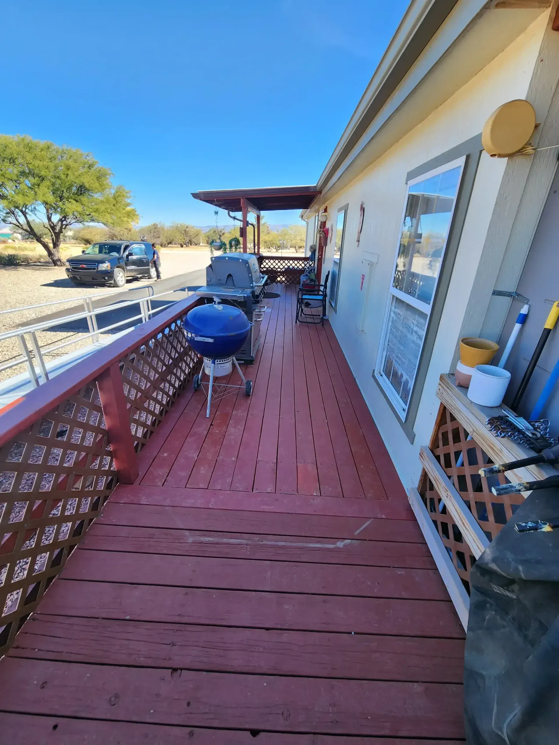 Wooden deck with grill and railing next to a house under a clear sky.