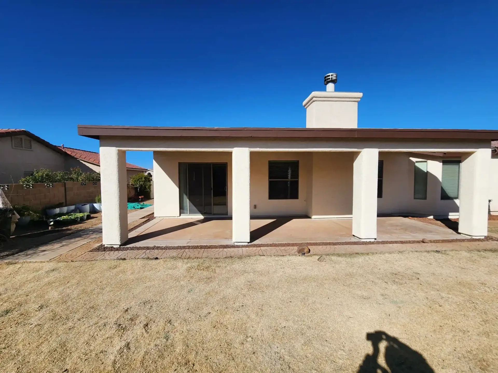 Backyard patio with a brown roof and white pillars against a clear blue sky.