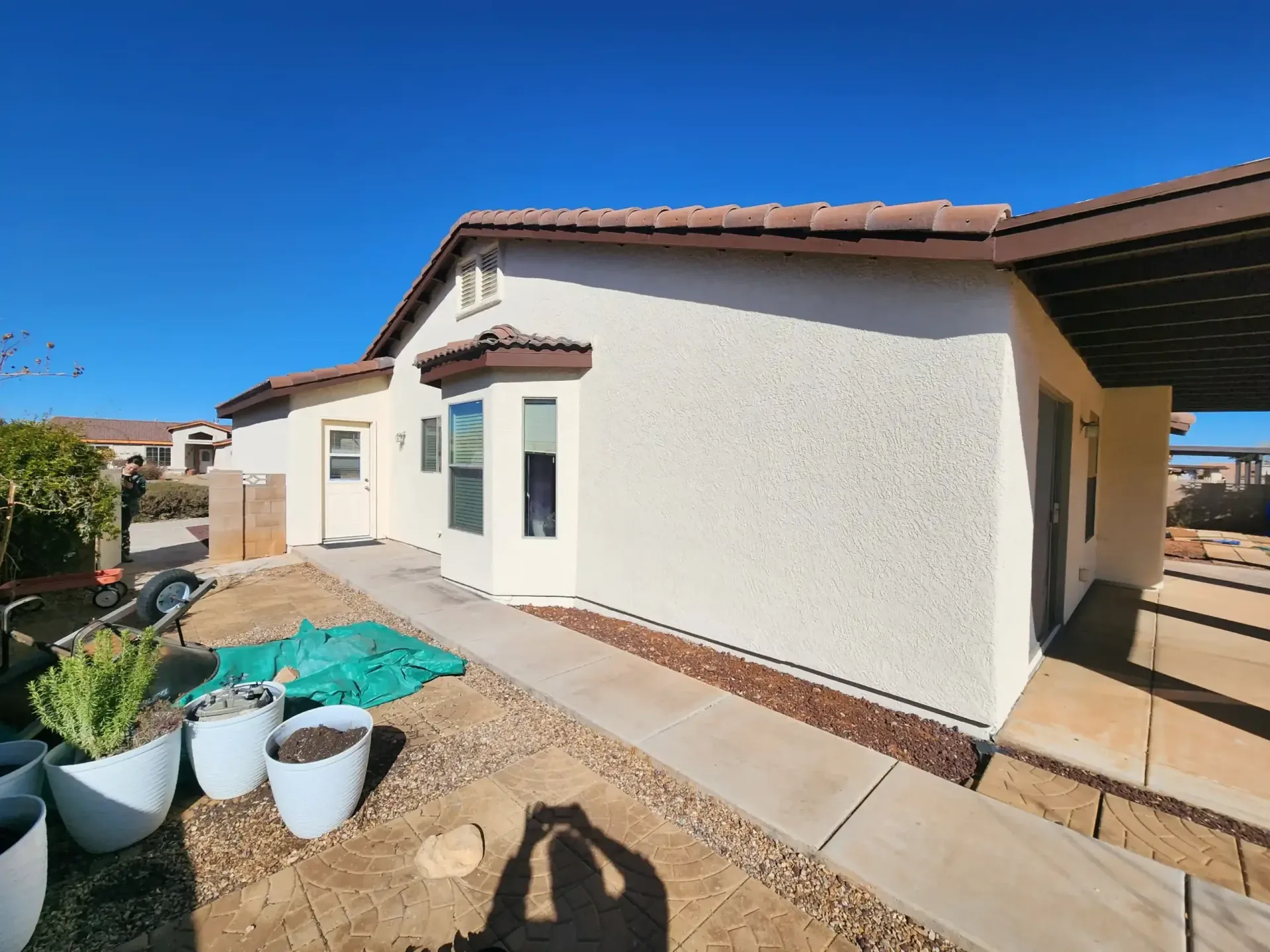 Exterior view of a stucco house with a tiled roof, patio, and blue sky.