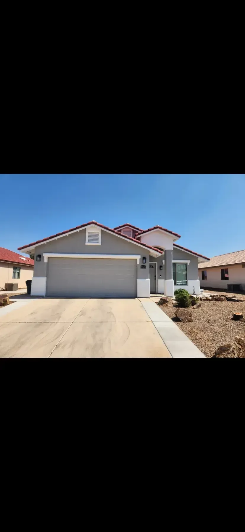 Gray house with a two-car garage, white trim, and a red tile roof on a sunny day.