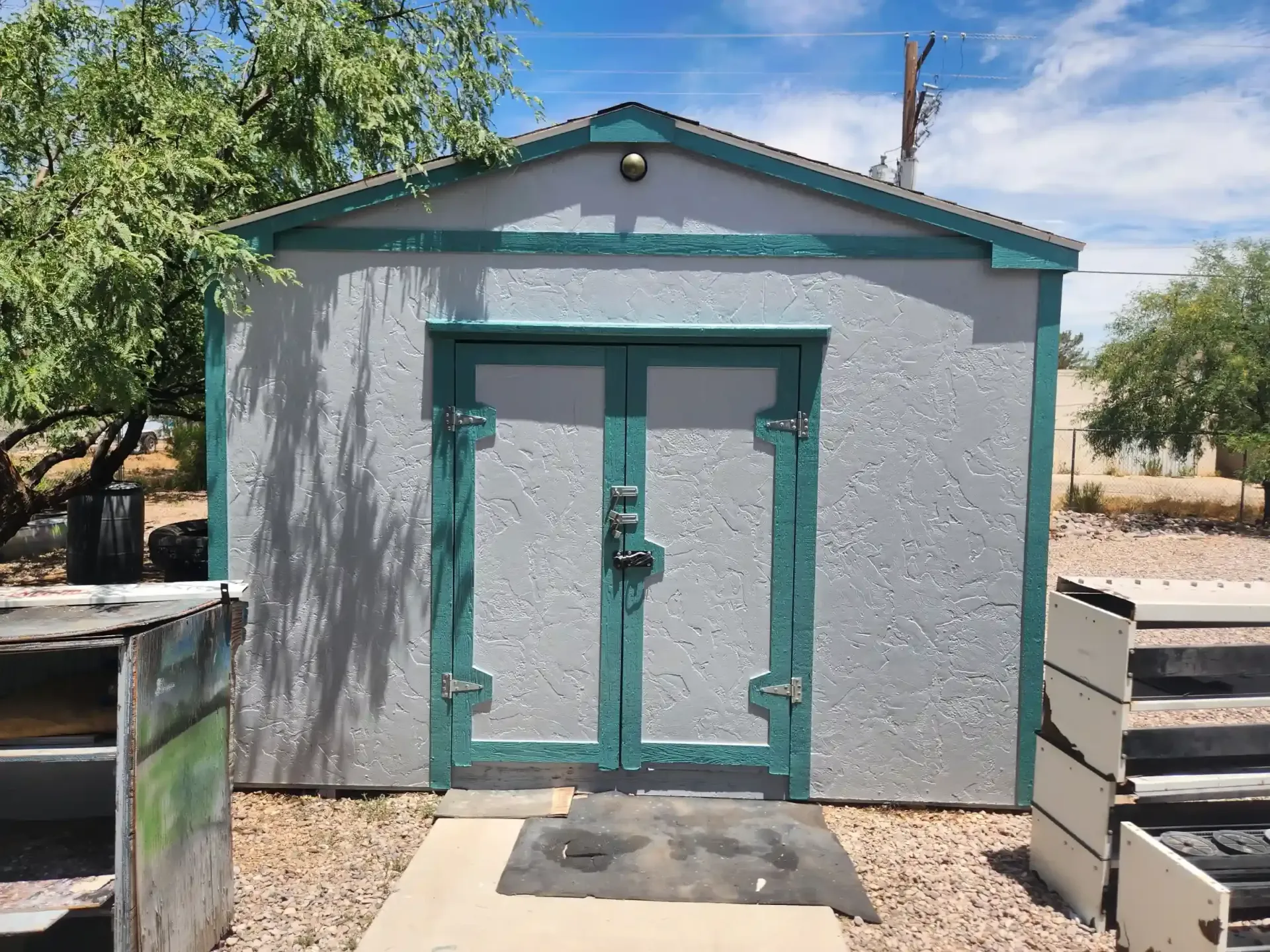Gray shed with teal trim and double doors on a sunny day.