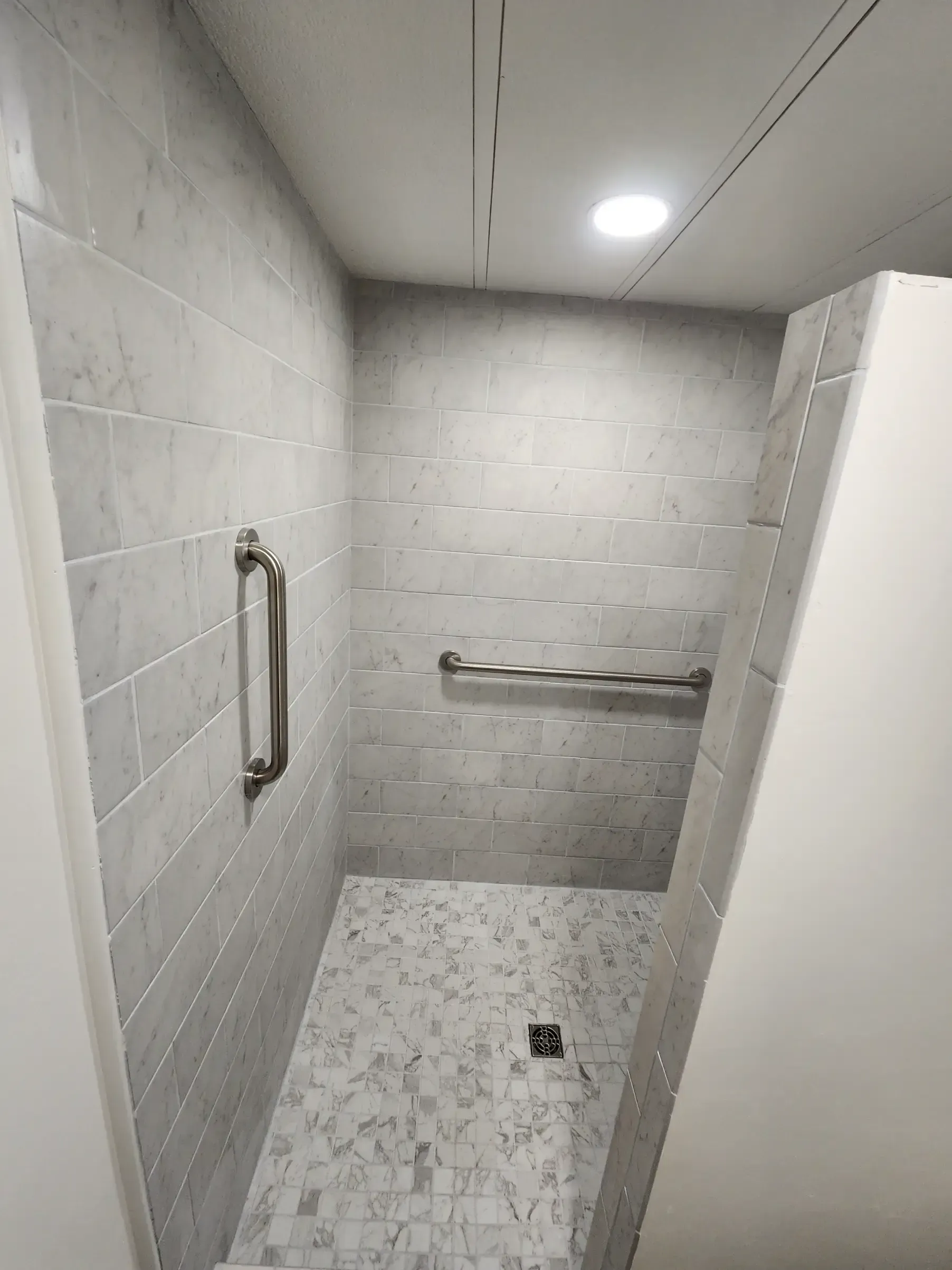 Accessible shower with marble tile and grab bars.