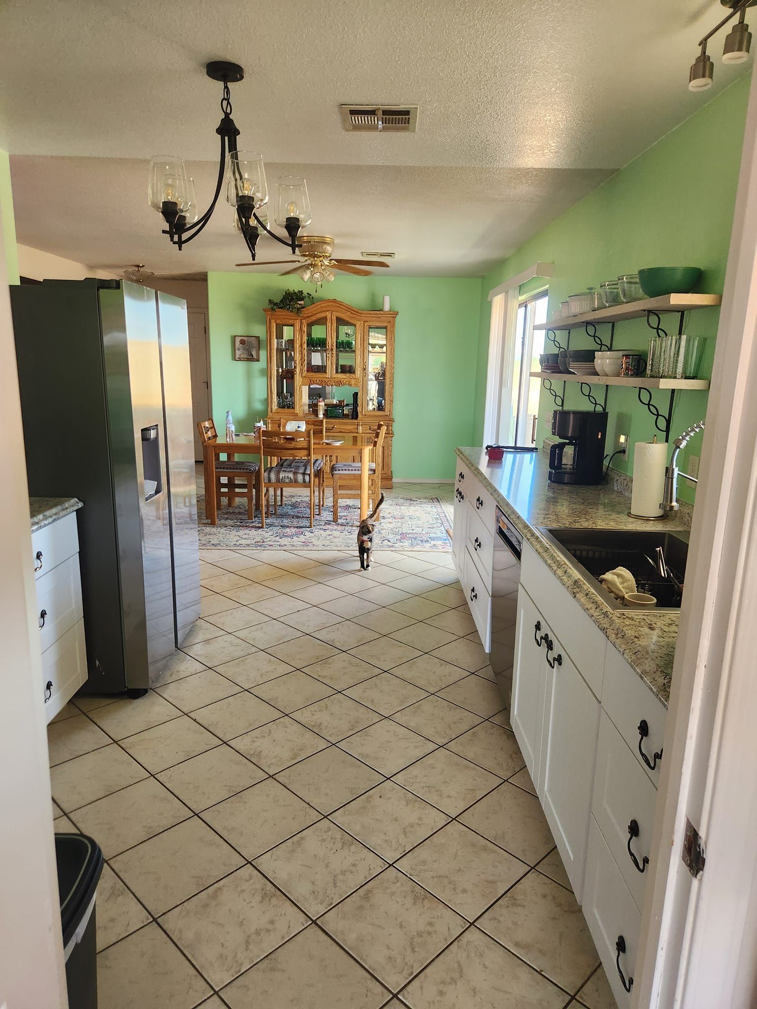 Kitchen with white cabinets, green walls, and dining area beyond.