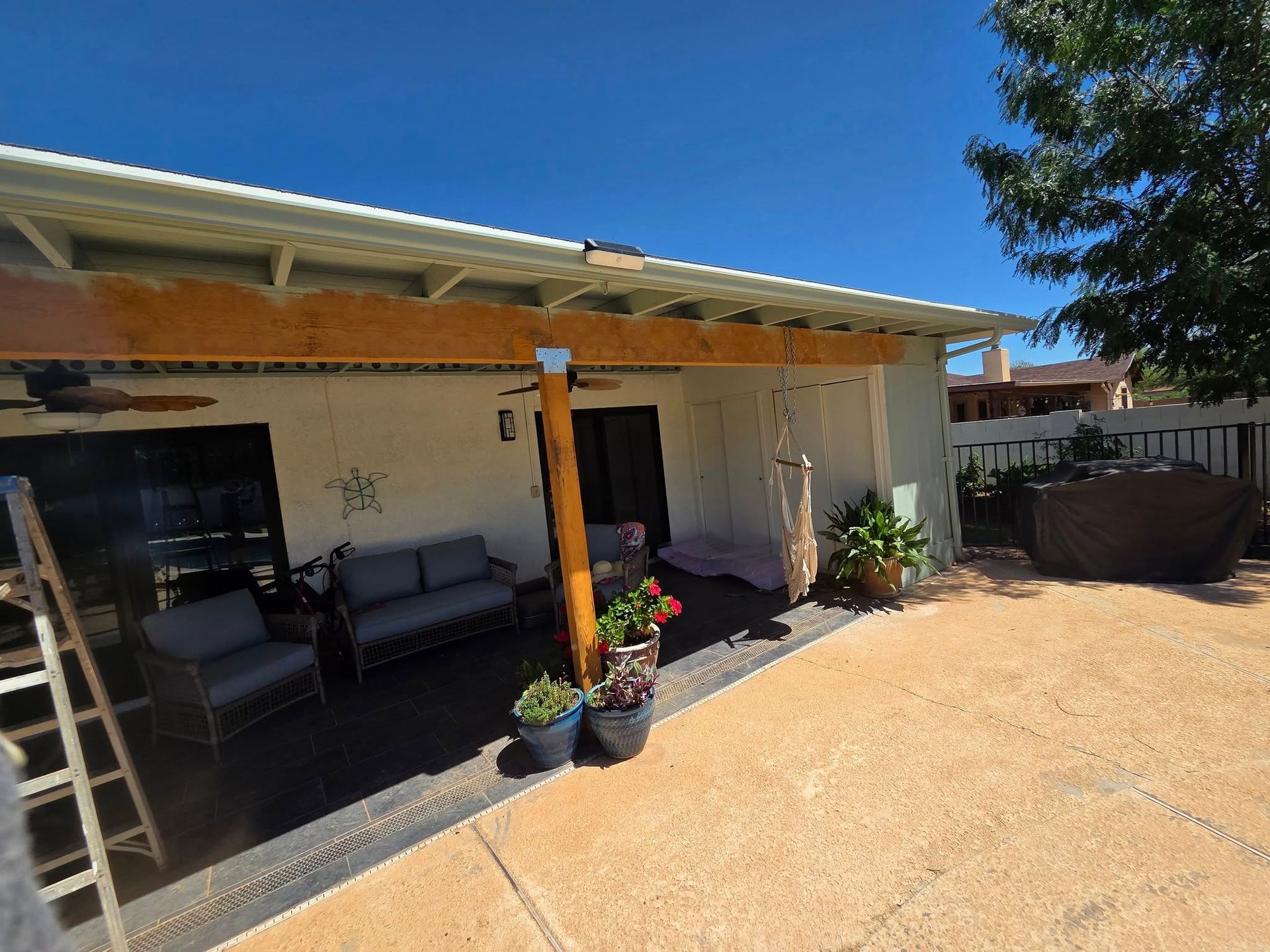 Backyard patio with wooden beams and a seating area, under a blue sky.