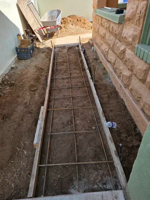 Concrete formwork with rebar, prepared for pouring concrete walkway alongside a building.