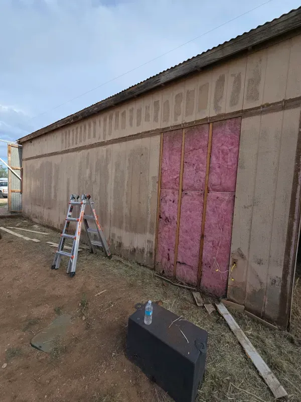 Exterior of a building under renovation, exposed insulation, ladder, and supplies on the ground.