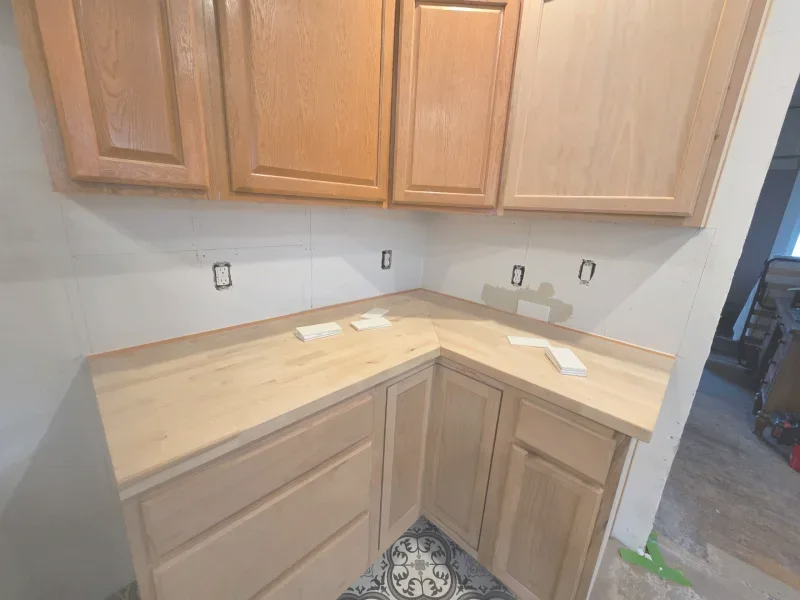 Kitchen cabinets and countertops; light wood, corner layout; electrical outlets visible; a work in progress.