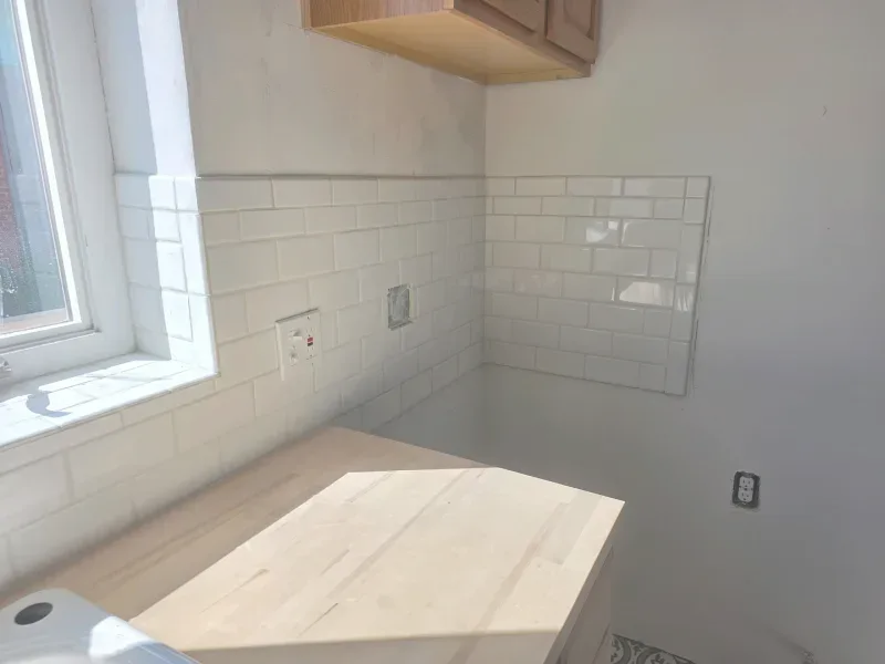 Kitchen corner with white subway tile backsplash, light-colored wood countertop, and window.