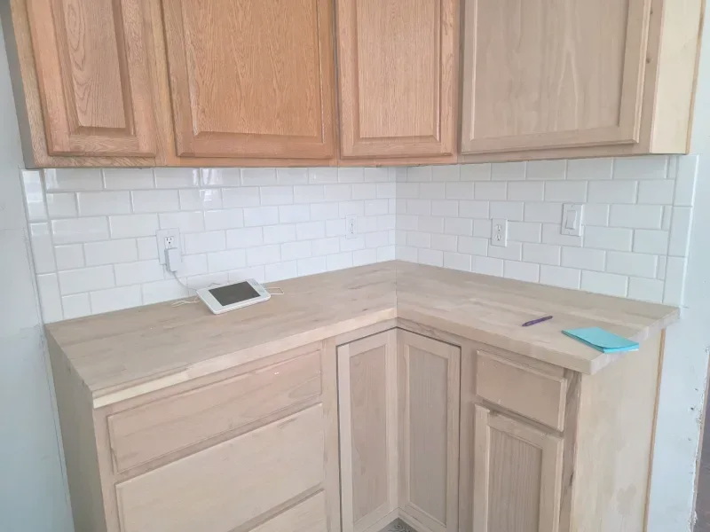 Kitchen corner with light wood cabinets and countertops, white subway tile backsplash.