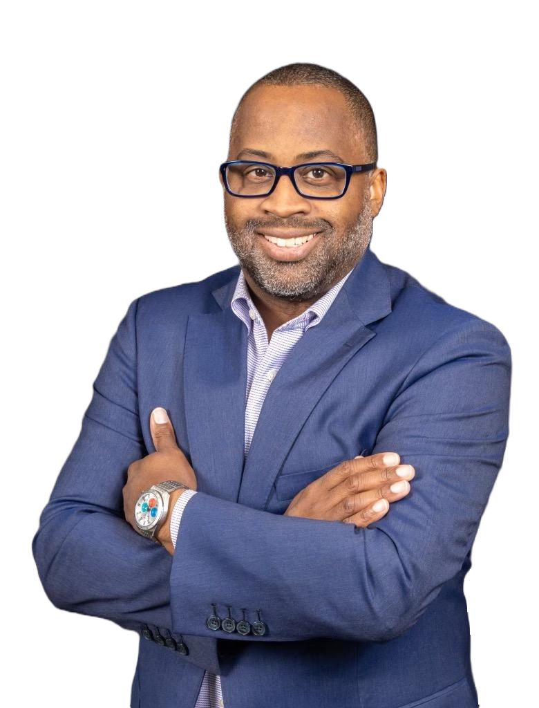 A man in a blue suit and glasses is standing with his arms crossed and smiling.