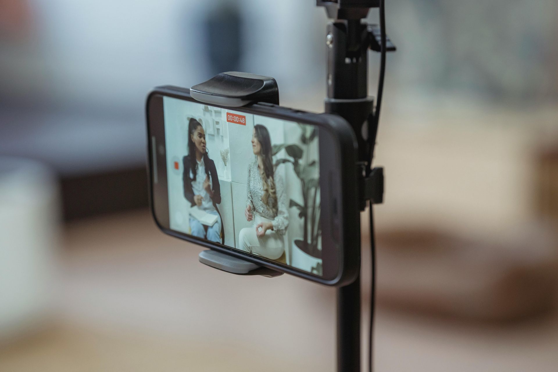 Smartphone on tripod displaying two women in conversation, recording video indoors.
