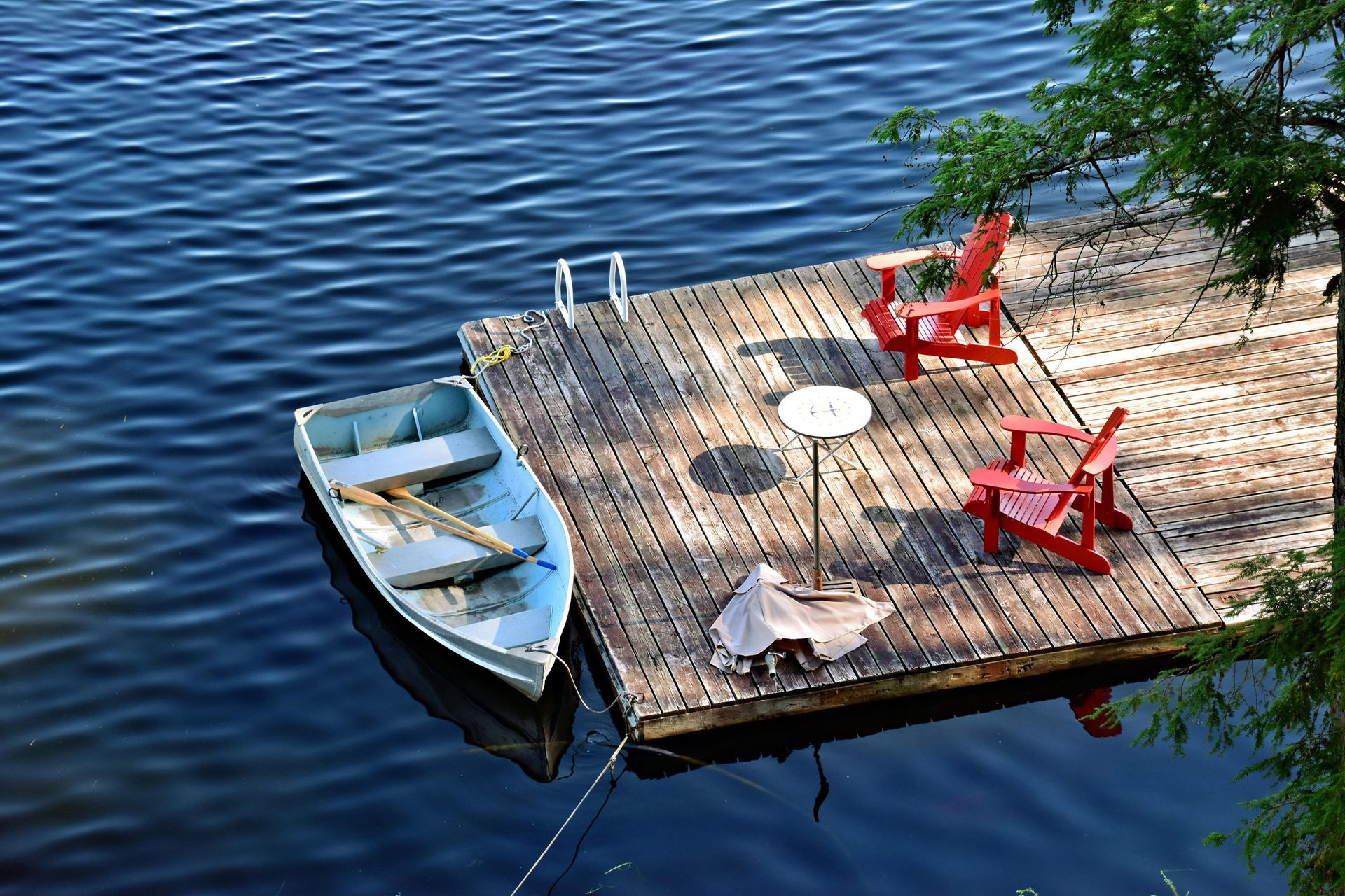 A person stands next to a truck pulling a dump trailer filled with brush on a gravel road surrounded by autumn trees.