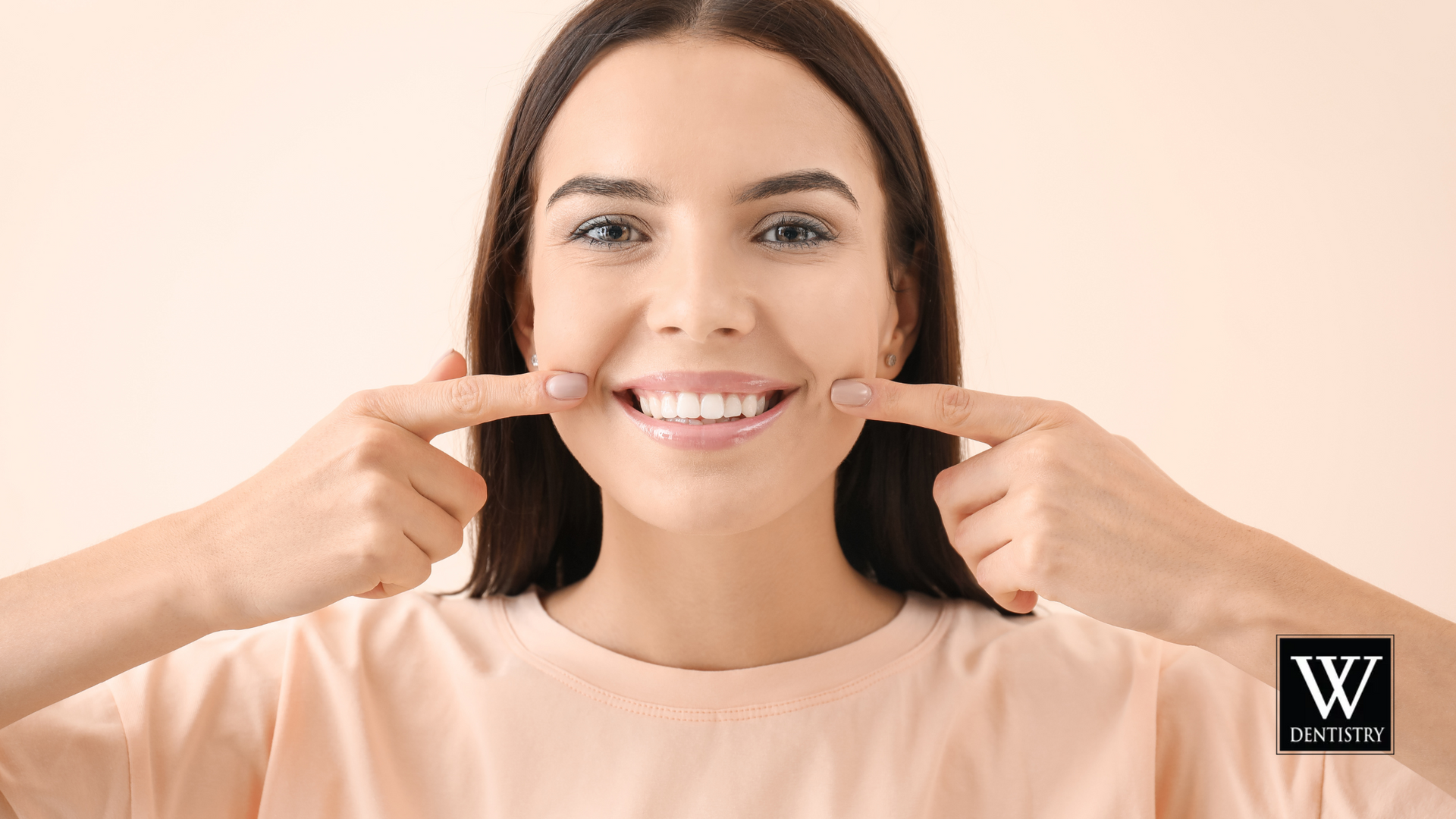 A woman is pointing at her teeth and smiling.