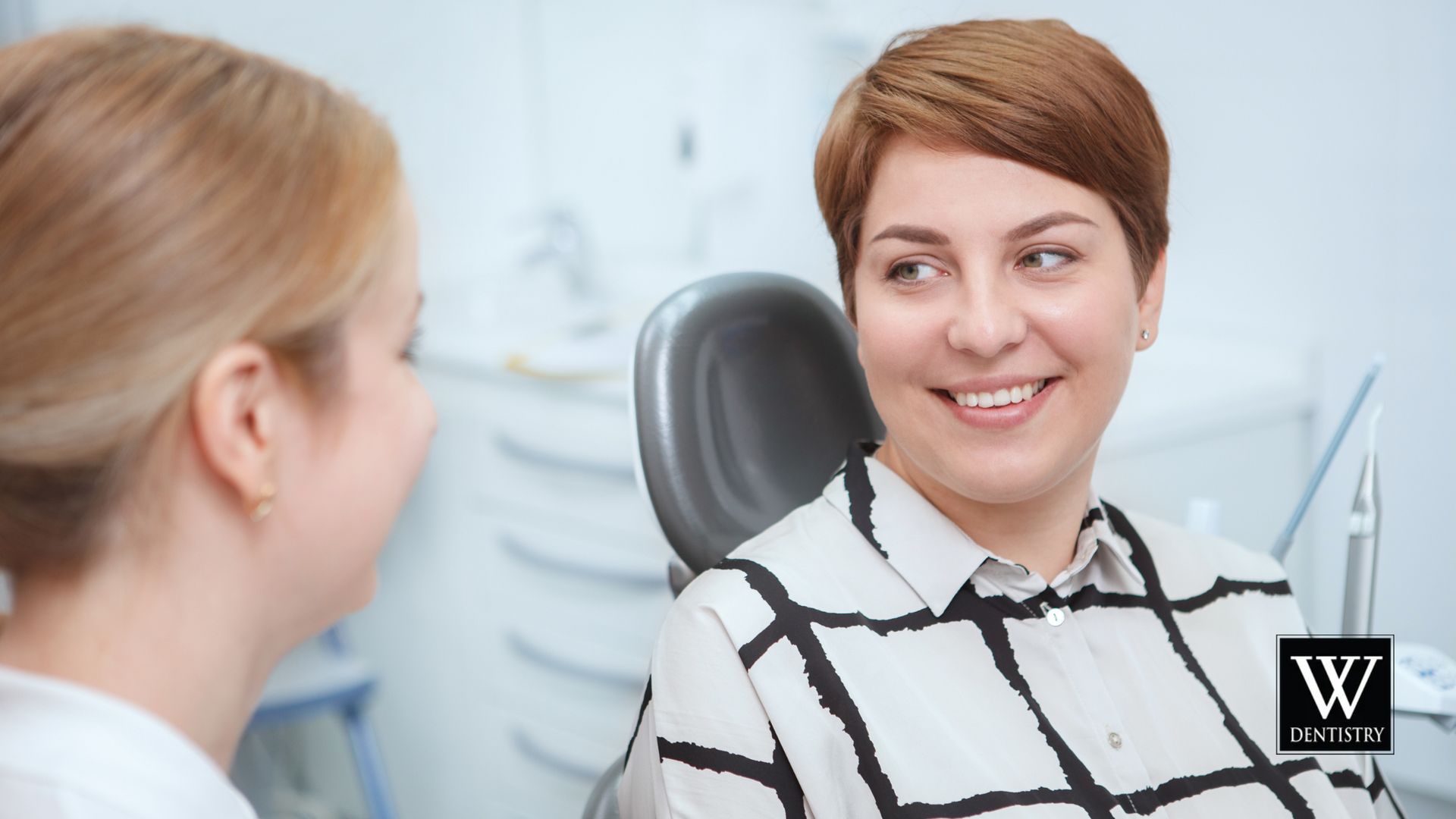 A woman is sitting in a dental chair talking to a dentist.