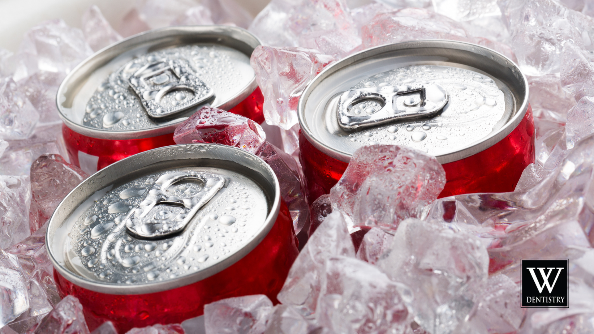 Three silver soda cans in crushed ice, red labels visible, with a small black logo in the corner